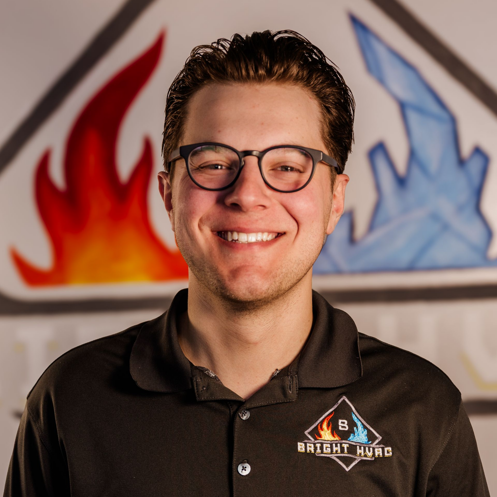 Smiling person in glasses wearing a black Bright Hound shirt, with red flame and blue ice artwork behind them.