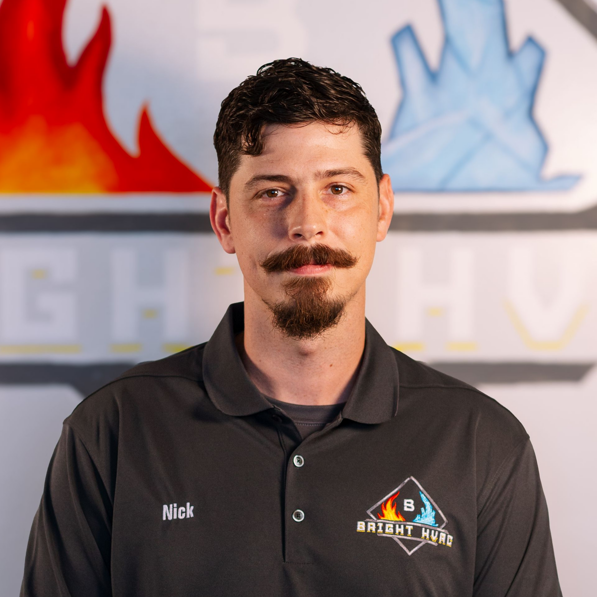 Portrait of a man in a dark polo shirt with a logo, standing before a blurred fire-and-ice sign