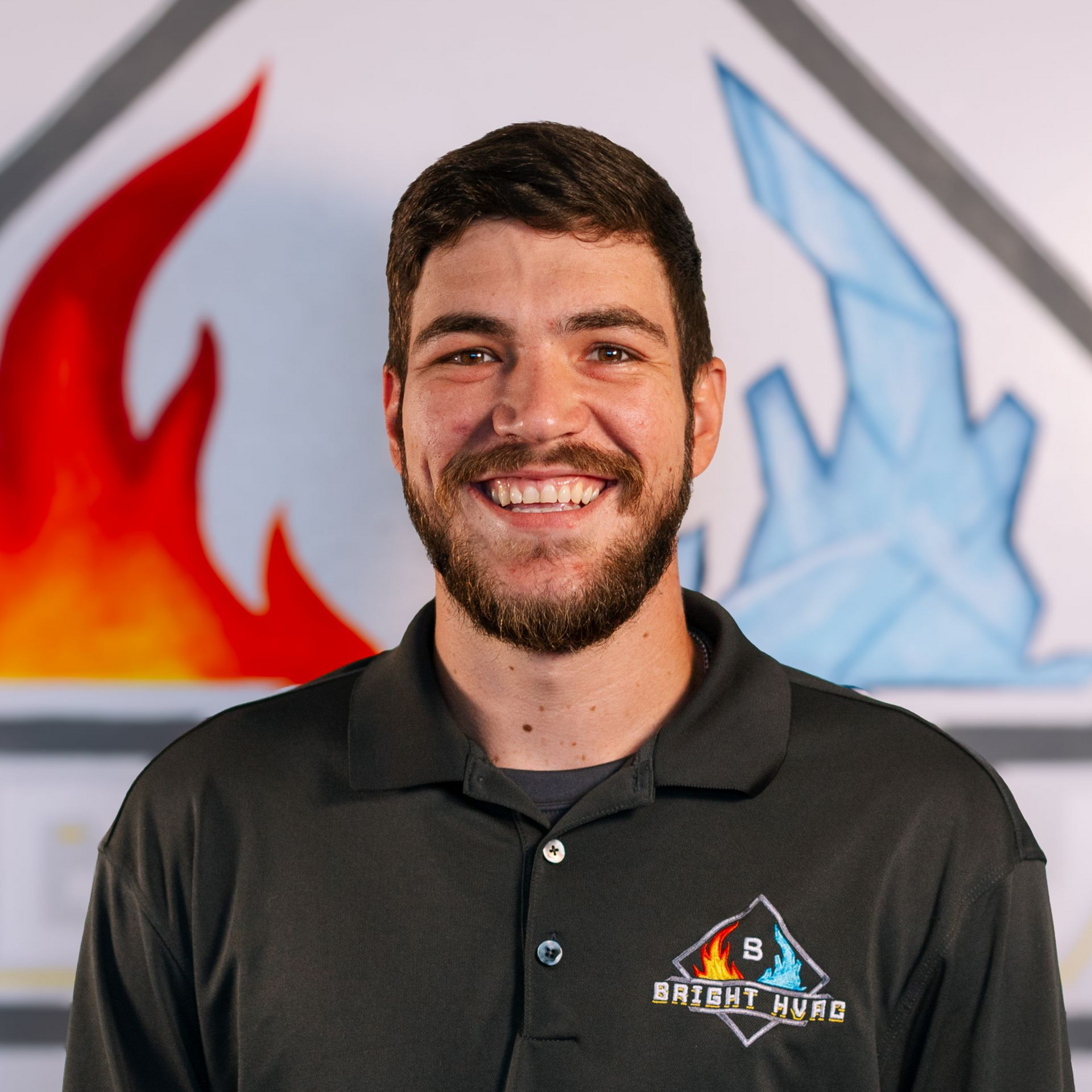 Smiling man in a black polo with a logo, standing before red and blue flame graphics