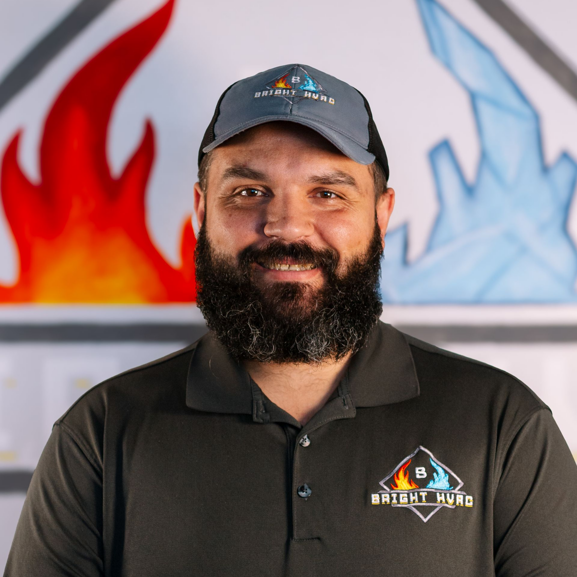 Smiling bearded man in black polo and cap with BrightView logo, standing before colorful wall art