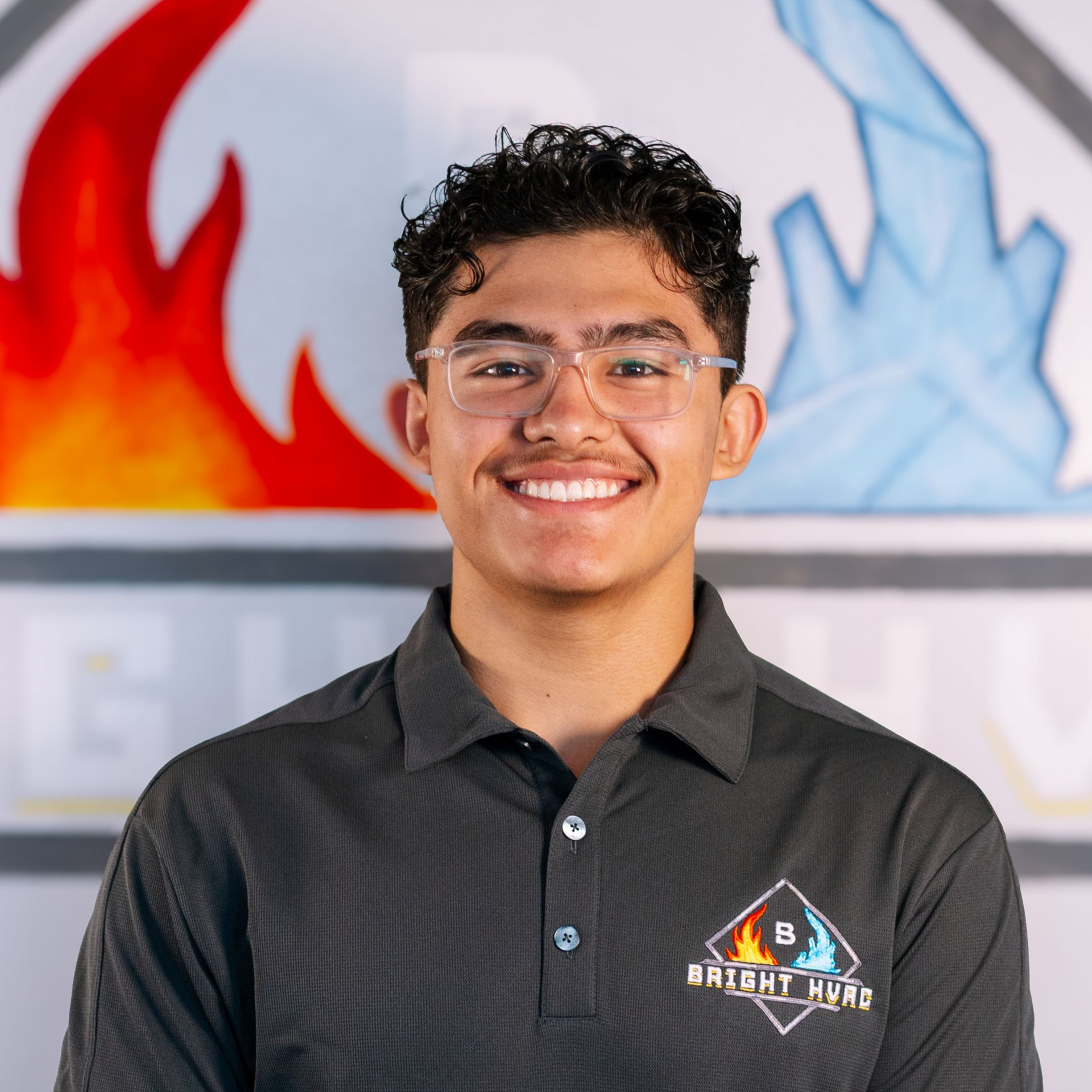 Smiling person in glasses and a dark polo shirt standing before a red and blue wall mural