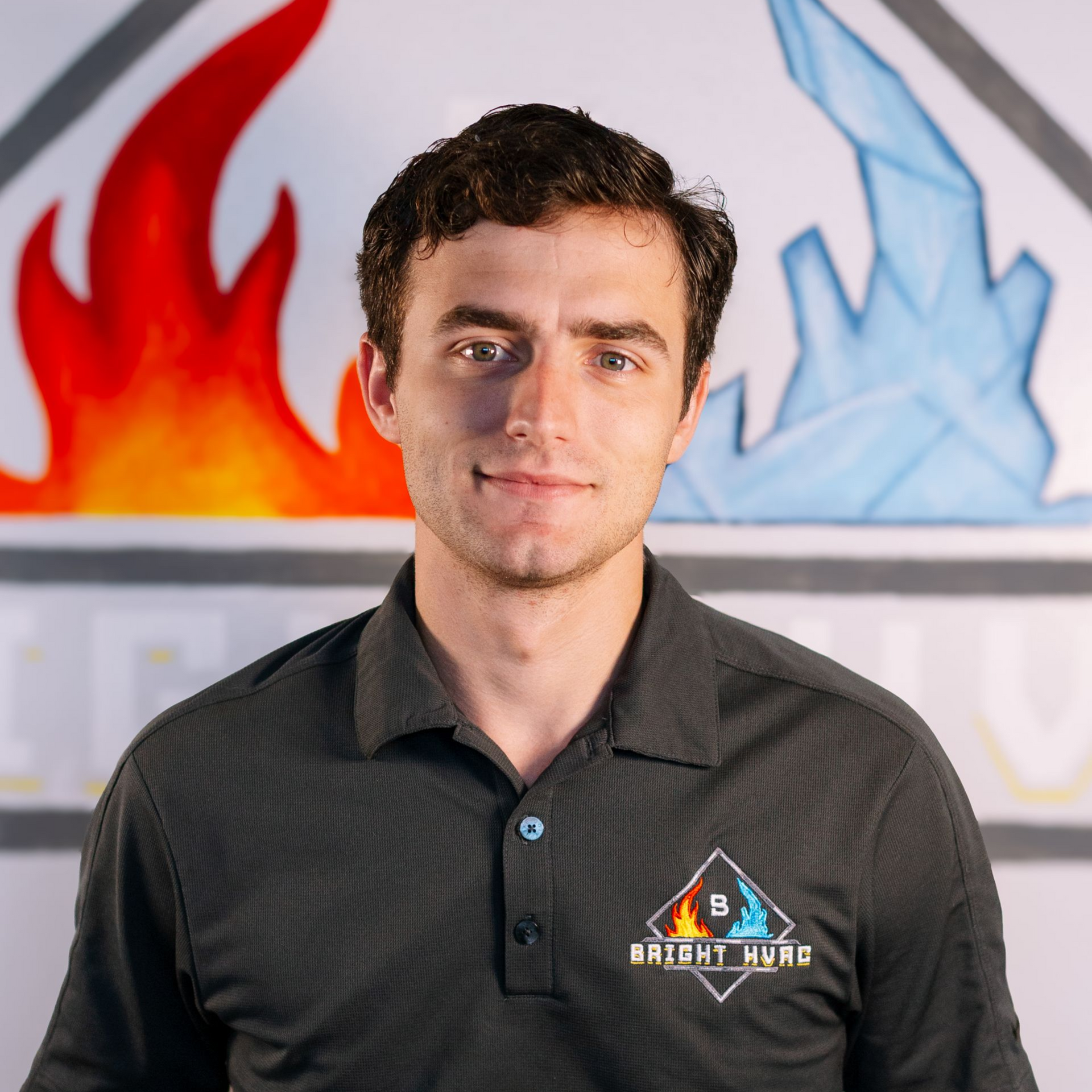 Man in a black polo shirt standing in front of a red and blue flame graphic background