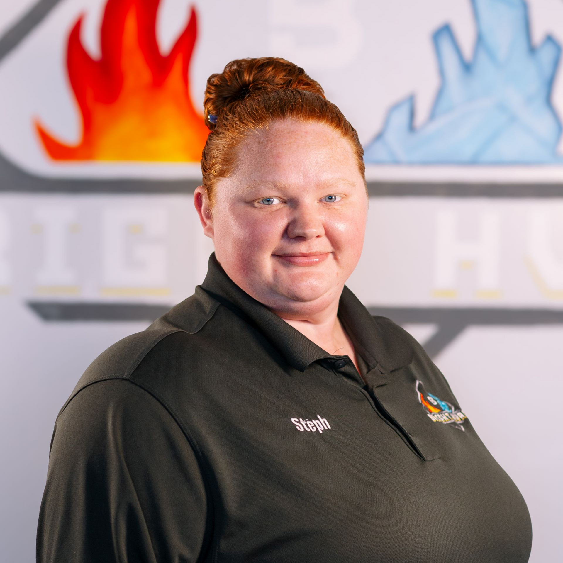 Portrait of a smiling woman in a black polo shirt standing before a blurred office logo wall.