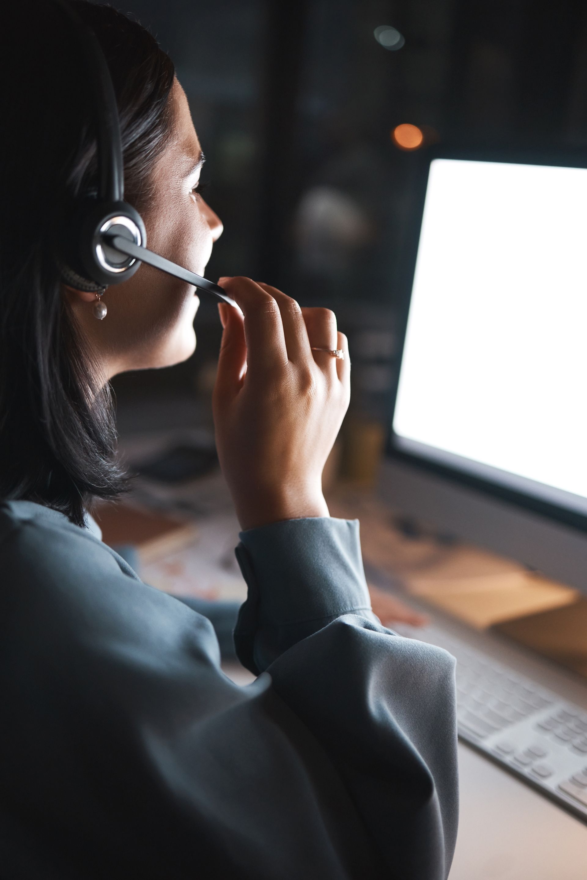 A woman wearing a headset is sitting in front of a computer.
