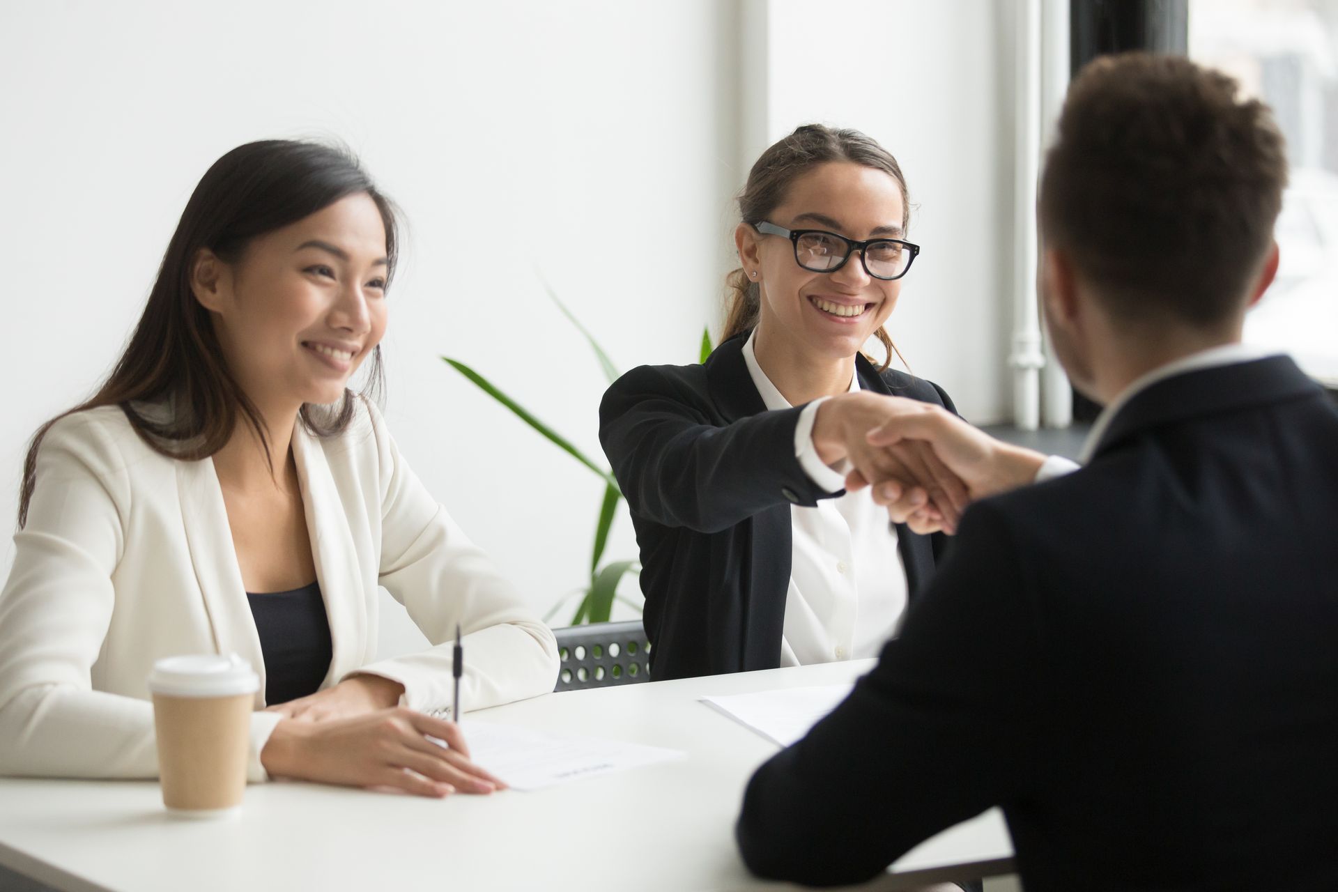 A man and two women are shaking hands during a job interview.