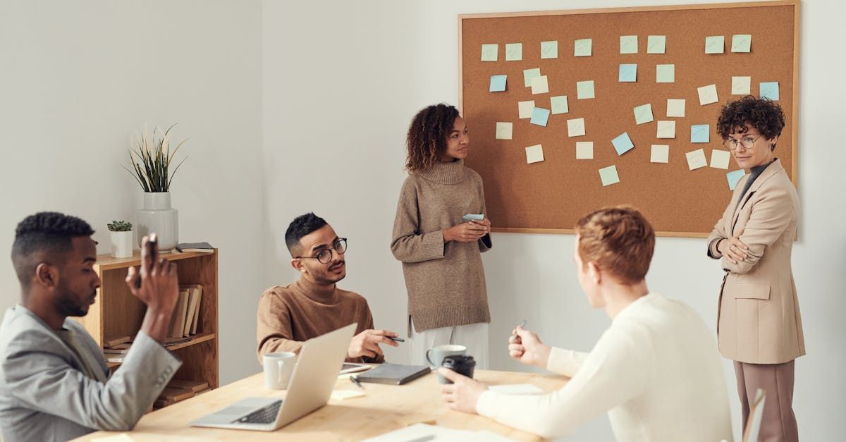 A group of people are sitting around a table in front of a cork board.
