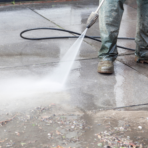 Person power washing a concrete patio with a high-pressure hose.