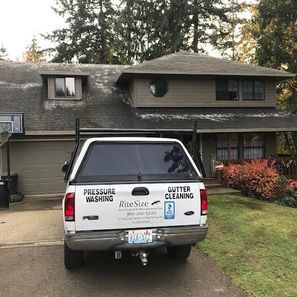 White pickup truck with business signage parked in front of a two-story house, advertising pressure washing and gutter cleani