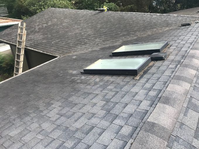 Dark gray asphalt shingle roof with two skylights. A ladder is visible.