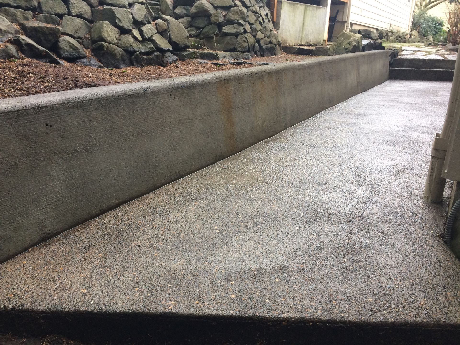 Concrete ramp sloping down from a retaining wall with rock and dirt above.