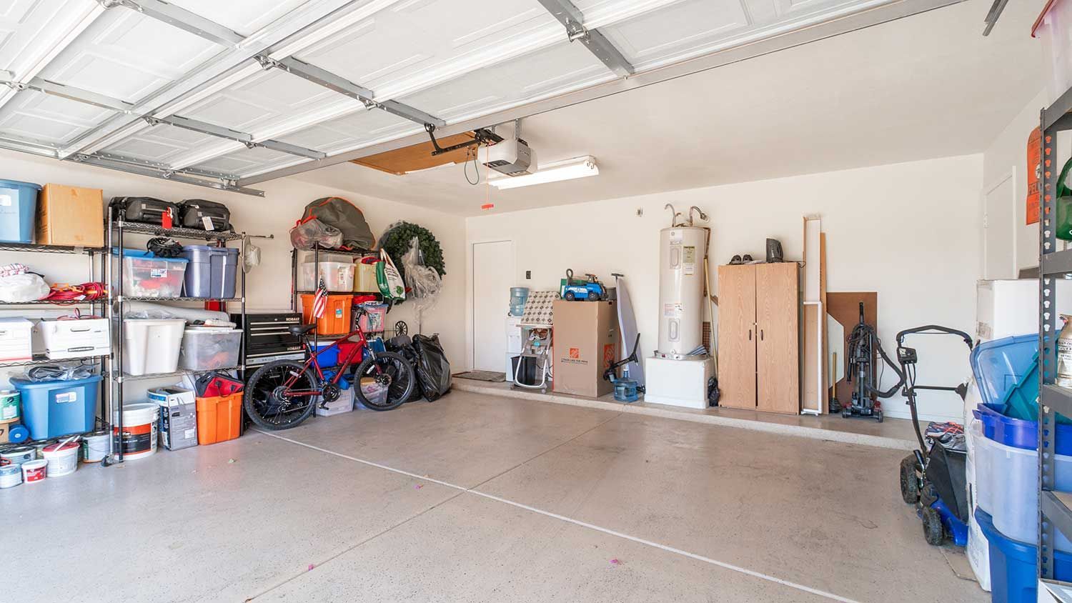 Garage interior with shelving, storage, and a water heater against a beige wall.