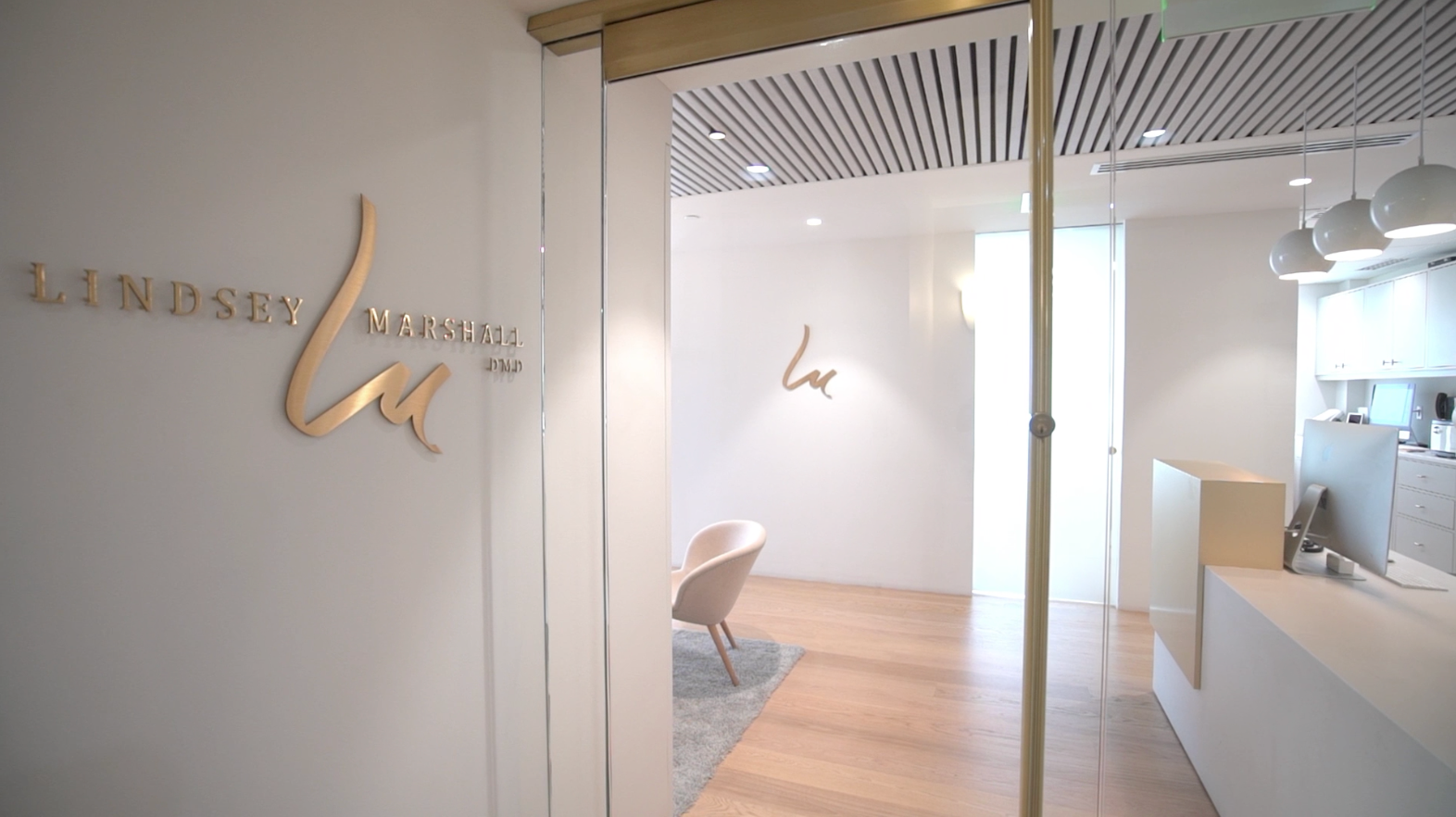 Entrance to a beauty clinic, with gold lettering, white walls, and a waiting area with a chair.