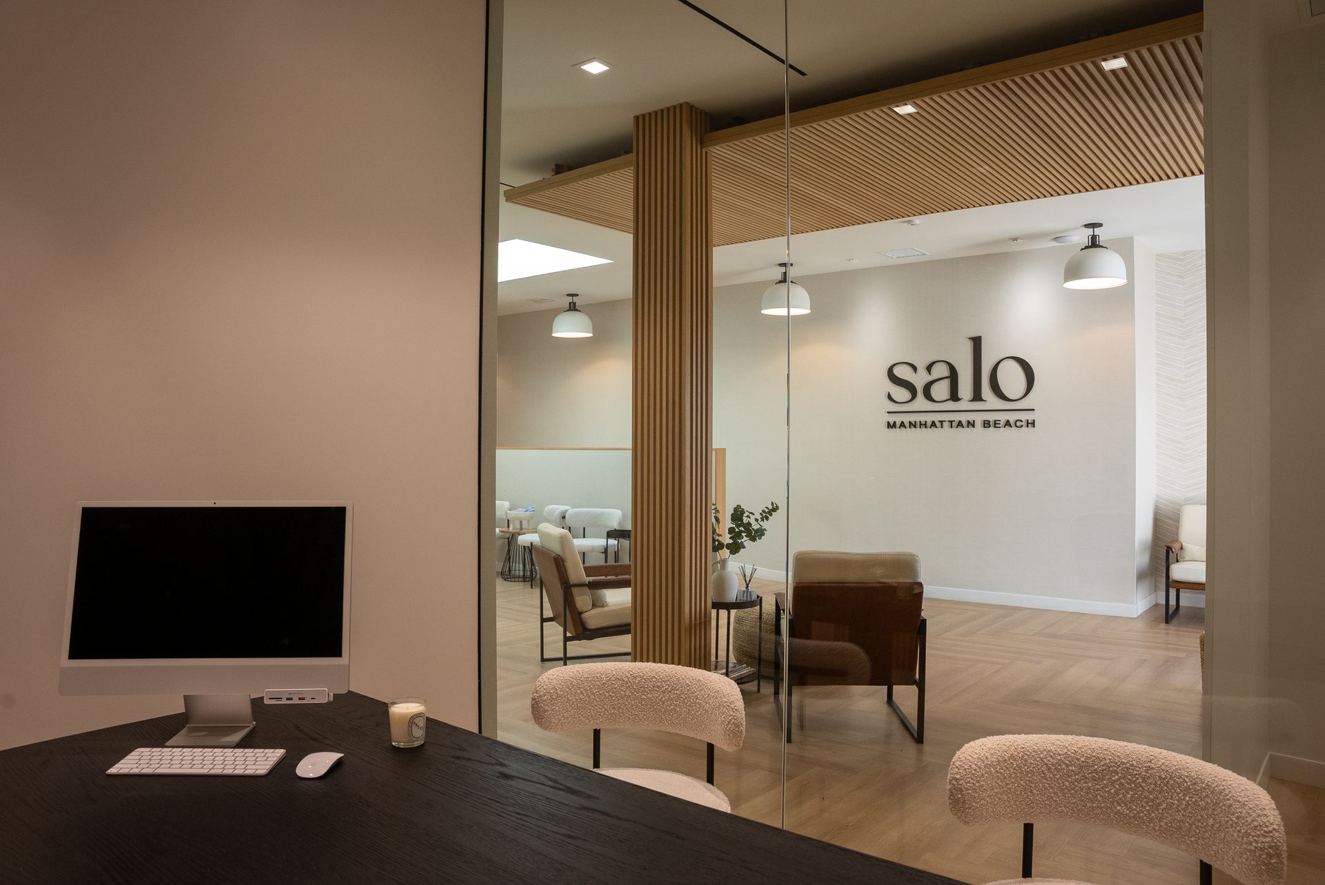 Office interior with a computer, chairs, and a view into a waiting area with the business name