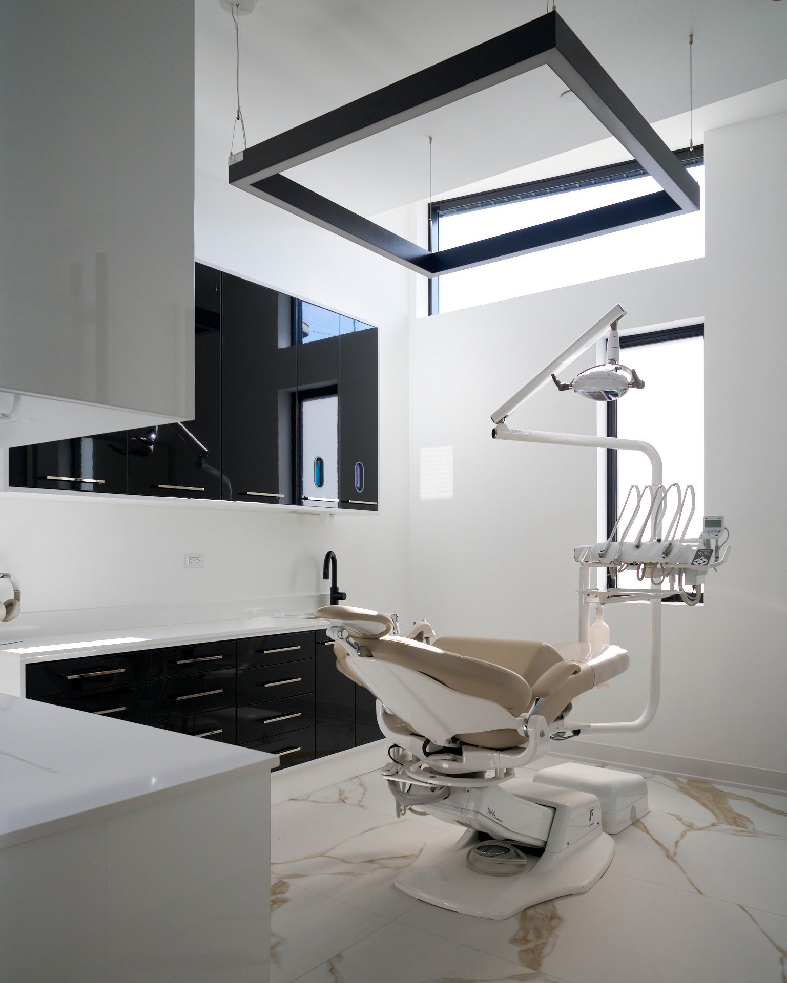 Modern dental office interior with beige dental chair, black cabinets, and white walls.
