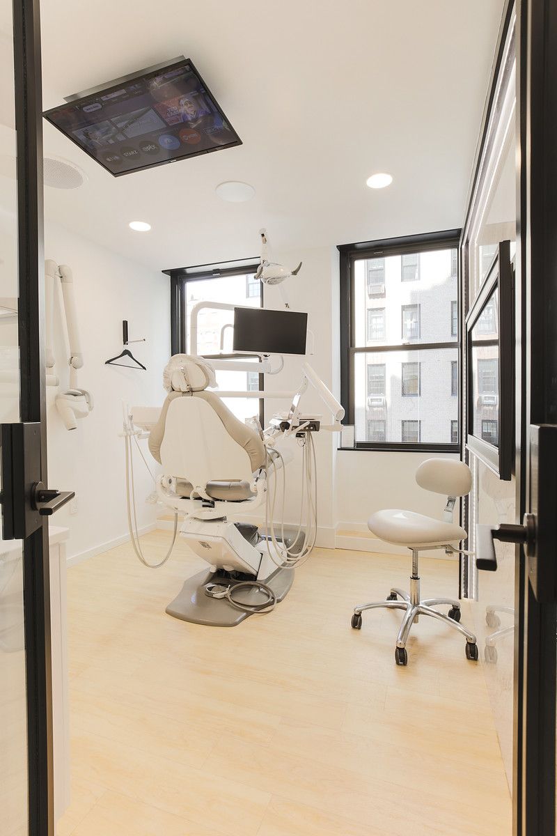 Bright dental exam room with chair, X-ray screen, stool, and large windows