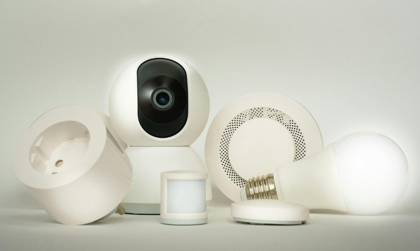 A camera , motion sensor , light bulb , and smoke detector are sitting on a table. A camera , motion sensor , light bulb , and smoke detector are sitting on a table.