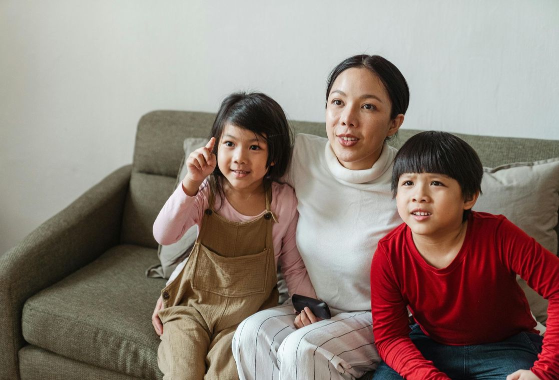 A woman and two children are sitting on a couch watching tv.