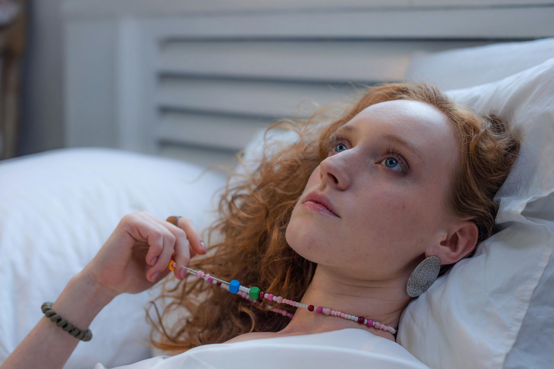 A woman is laying in bed with a necklace around her neck.