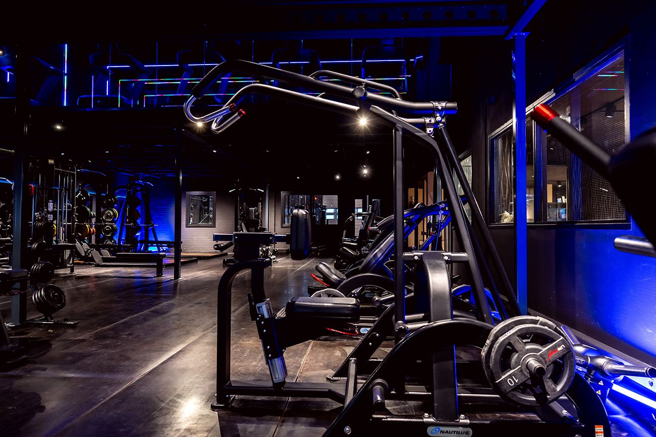 Interieur van de sportschool met gewichten, blauwe verlichting en een donkere omgeving.
