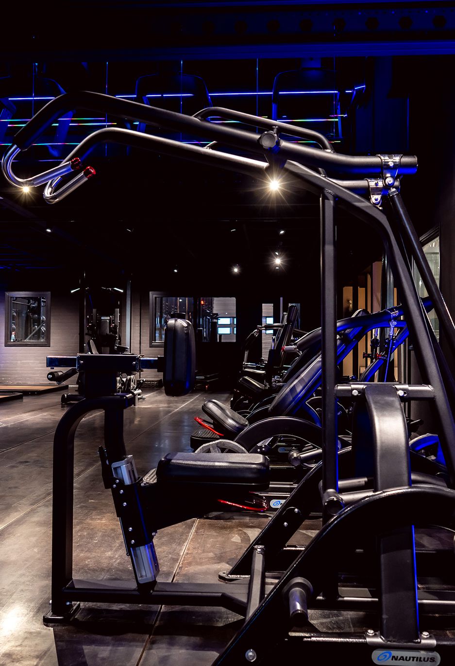 Interieur van de sportschool met gewichten, donkere, blauwe verlichting.