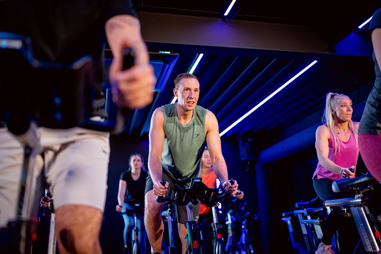 Mensen rijden op hometrainers in een donkere spinstudio met blauwe verlichting.