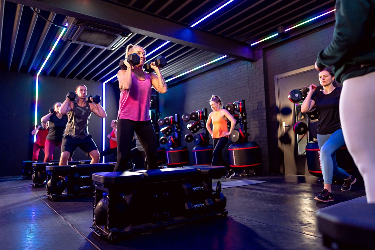Mensen trainen met gewichten op platforms in een sportschool met kleurrijke verlichting.