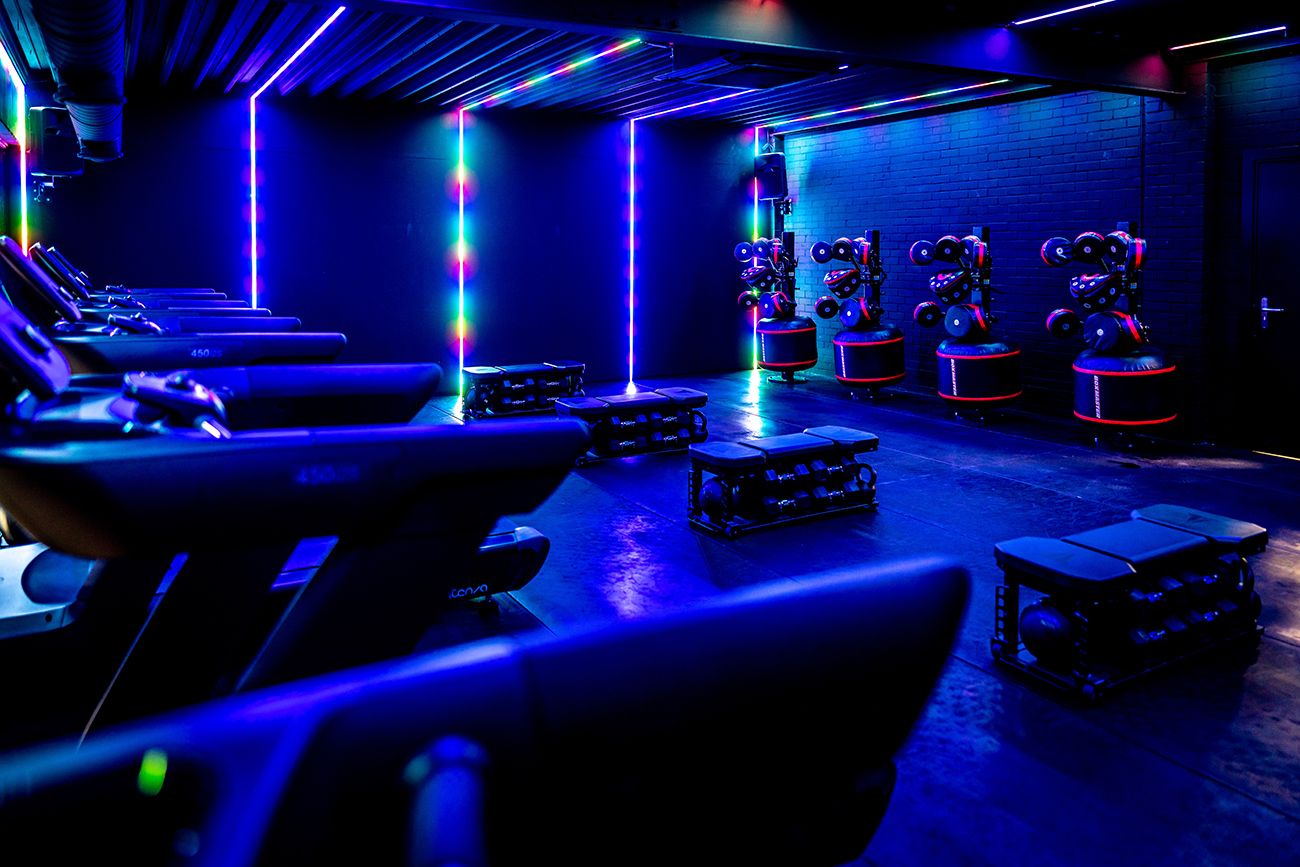 Een sportschool met veel fitnessapparatuur en blauwe verlichting.