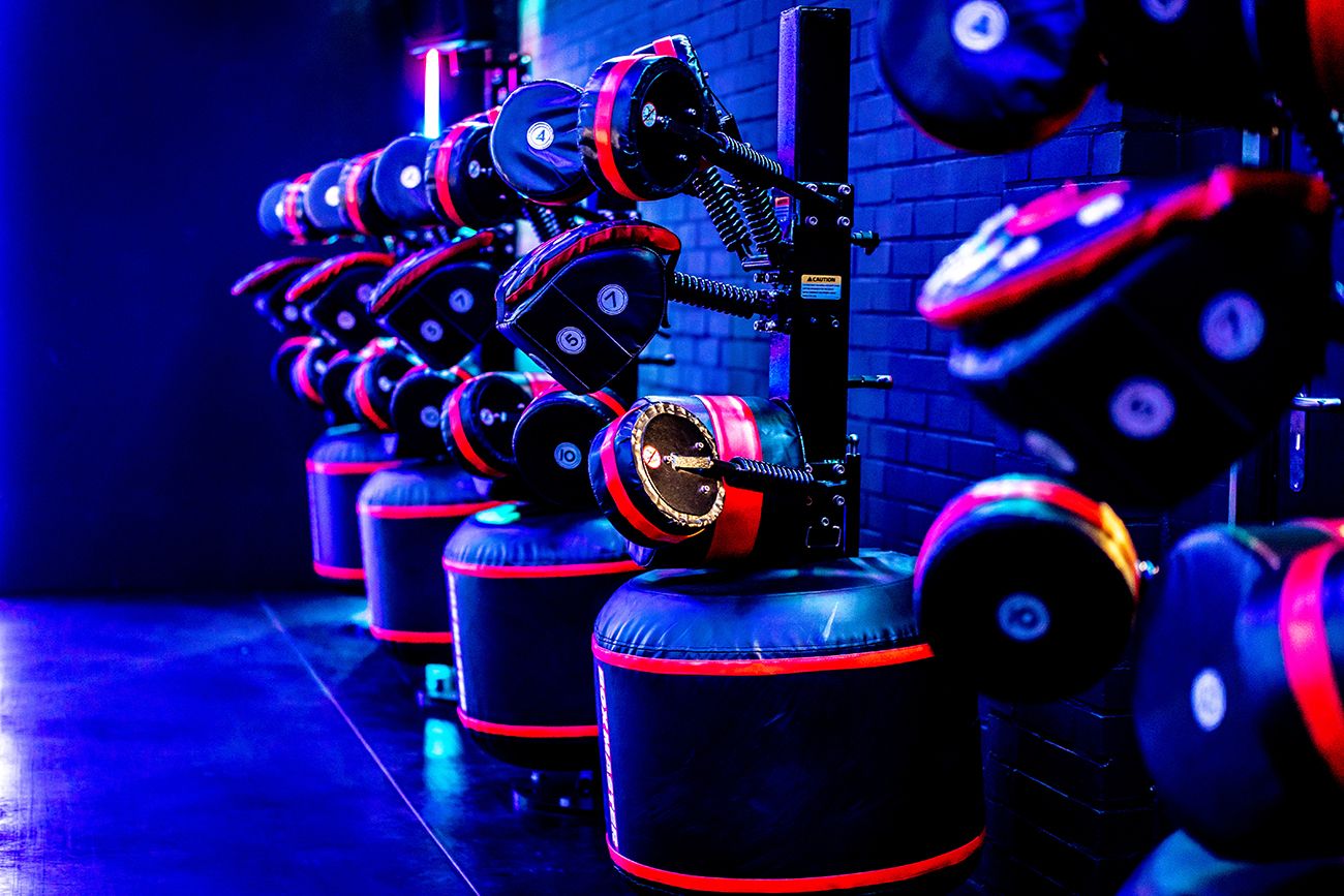 Een rij boksstations met zwarte en rode bokszakken in een blauw verlichte gymzaal.