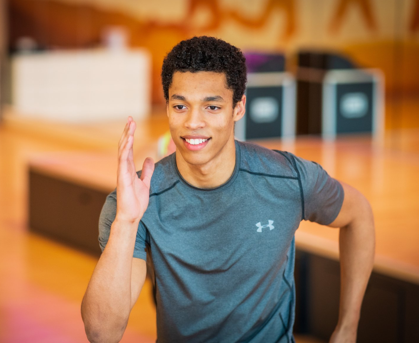Jongeman rent in een sportschool, draagt ​​een grijs shirt en lacht.