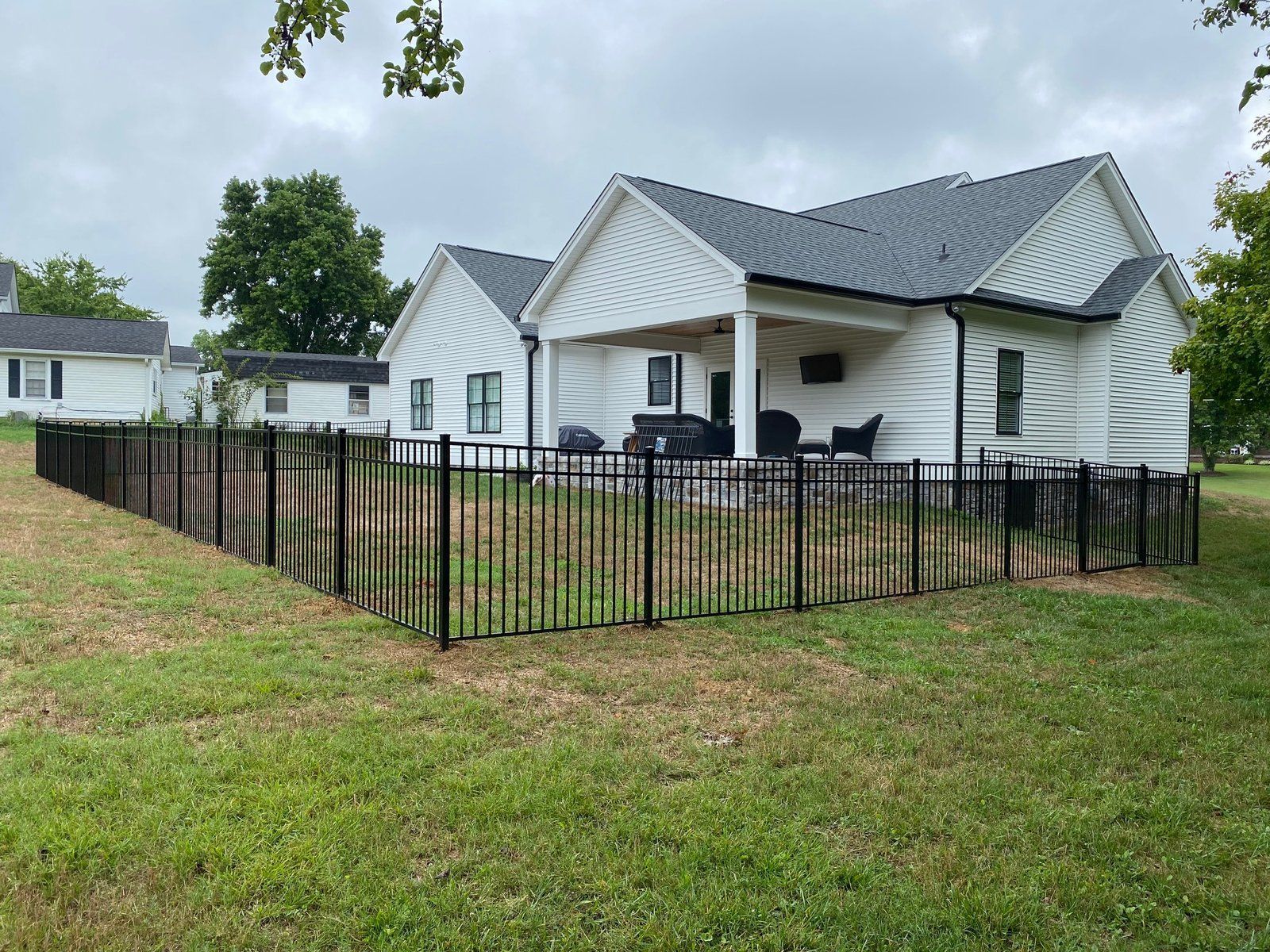 Black metal fence surrounding a white house with a porch and dark roof, on a grassy lawn.