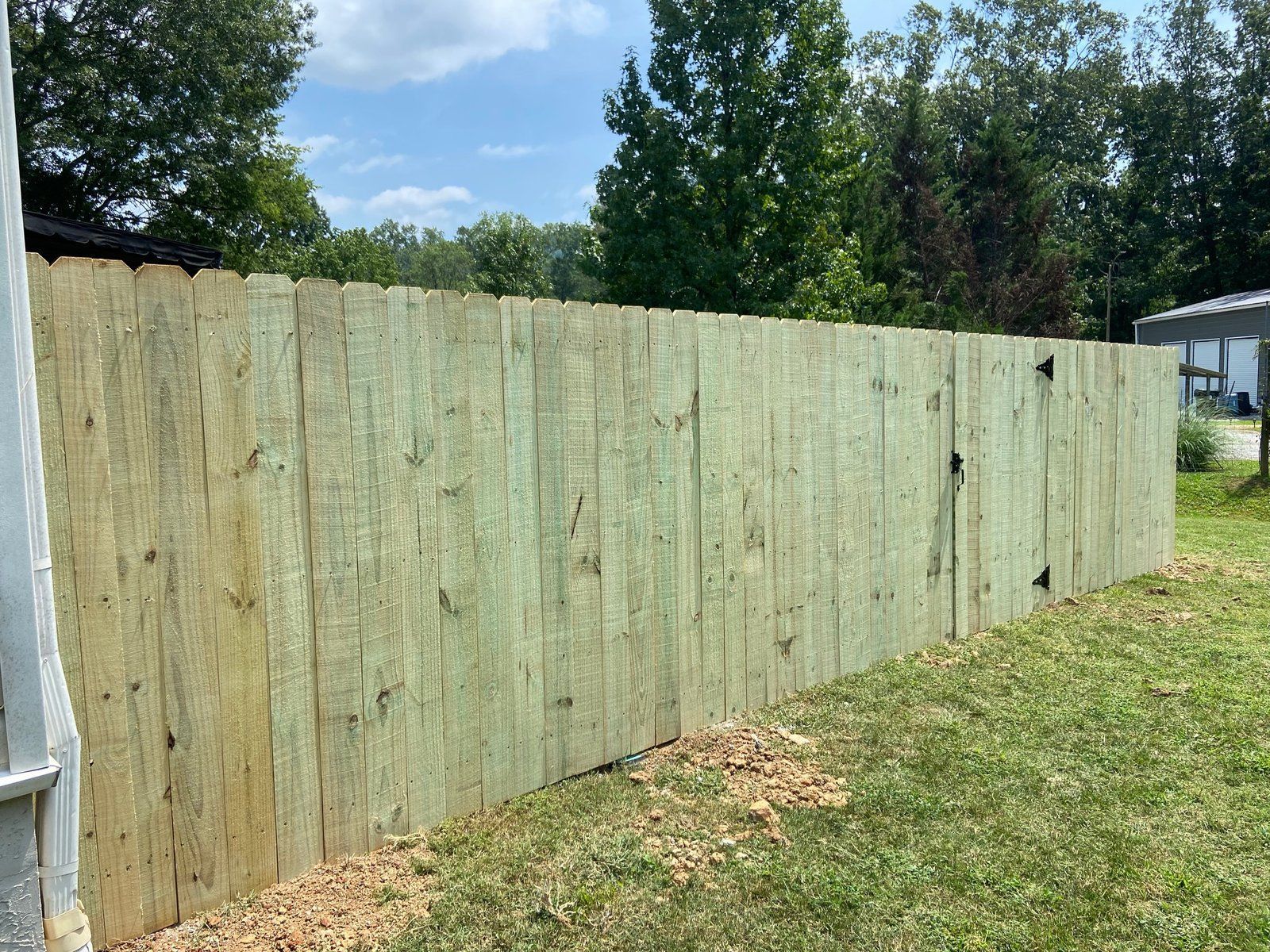 Wooden fence in a grassy yard, under a partly cloudy sky.