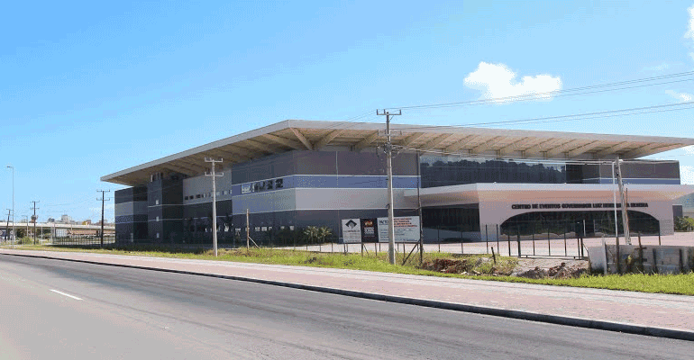 Edifício moderno com telhado plano, janelas grandes e uma estrada em primeiro plano. Céu azul.
