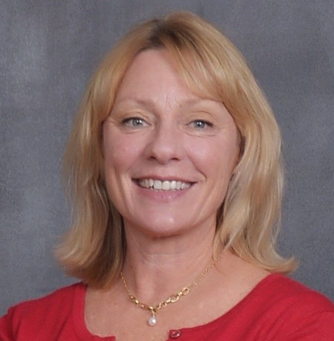 A woman wearing a red shirt and a gold necklace smiles for the camera