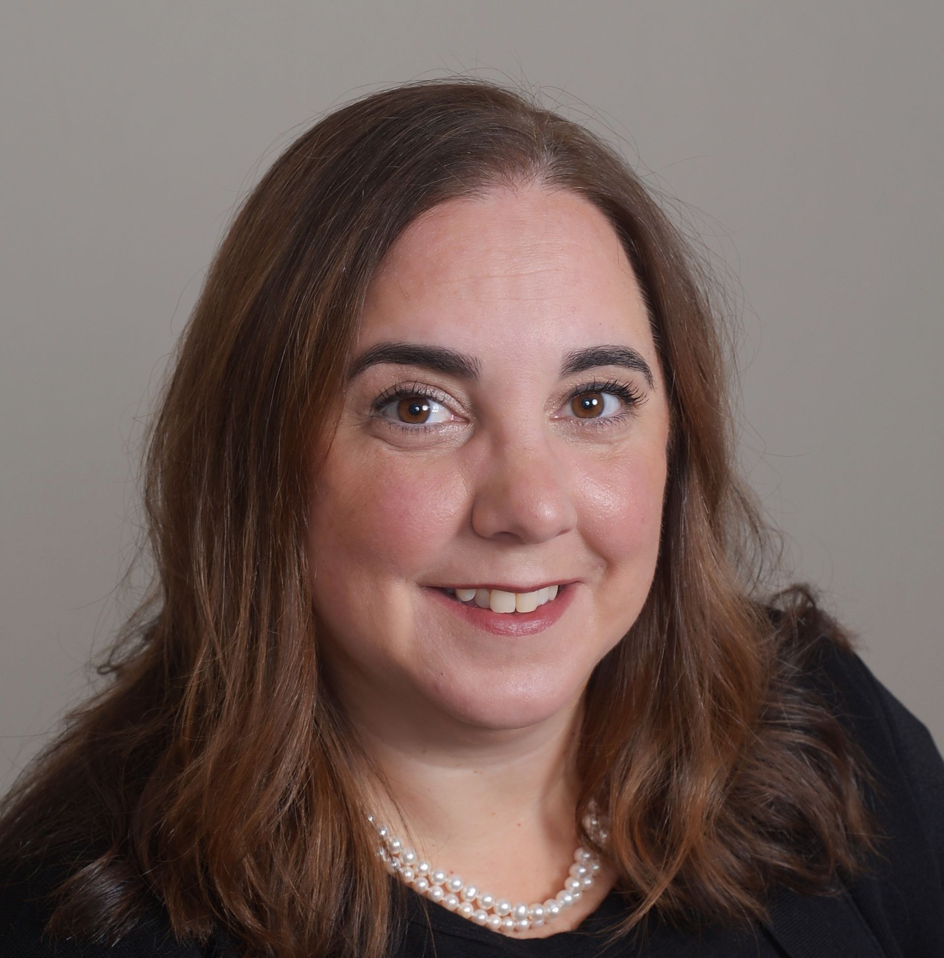 A woman wearing a black shirt and a pearl necklace is smiling for the camera.