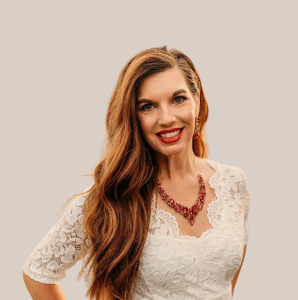 A woman with long hair is wearing a white lace top and a red necklace.