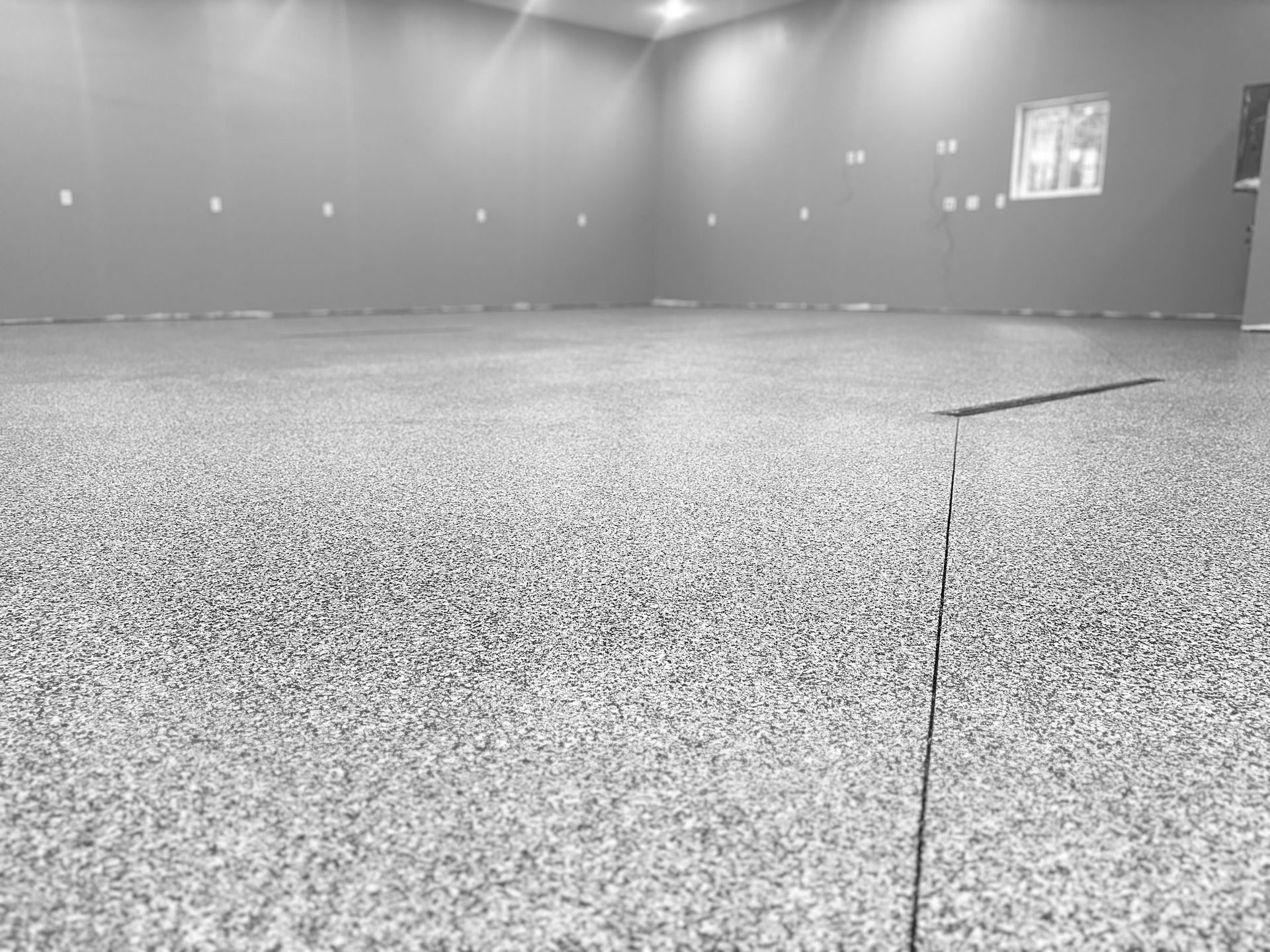 Empty gray indoor room with speckled carpet and wall lights, seen from a low angle.