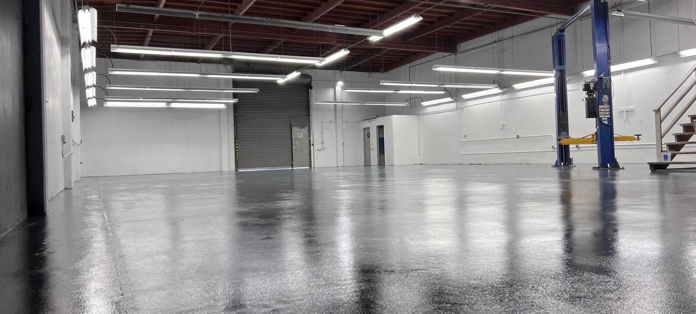 Empty industrial warehouse with polished concrete floor, white walls, and overhead red steel beams