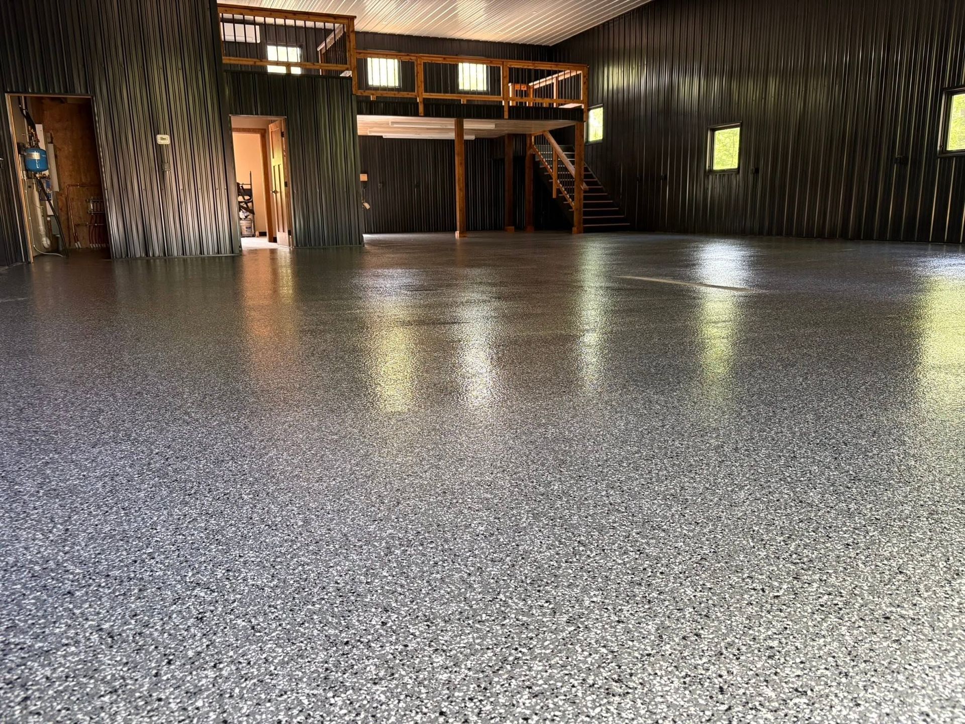 Empty indoor hall with a glossy speckled floor, dark walls, and a wooden mezzanine balcony.