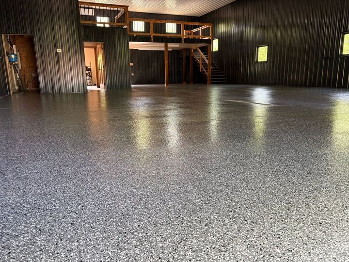 Empty indoor hall with a glossy speckled floor, dark walls, and a wooden mezzanine balcony.