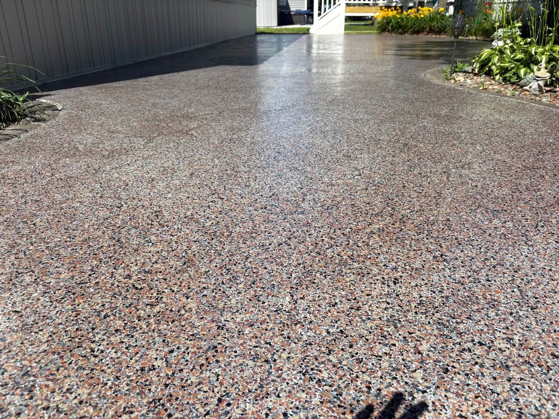 Pebbled walkway beside a building and garden, leading toward a bright patio area