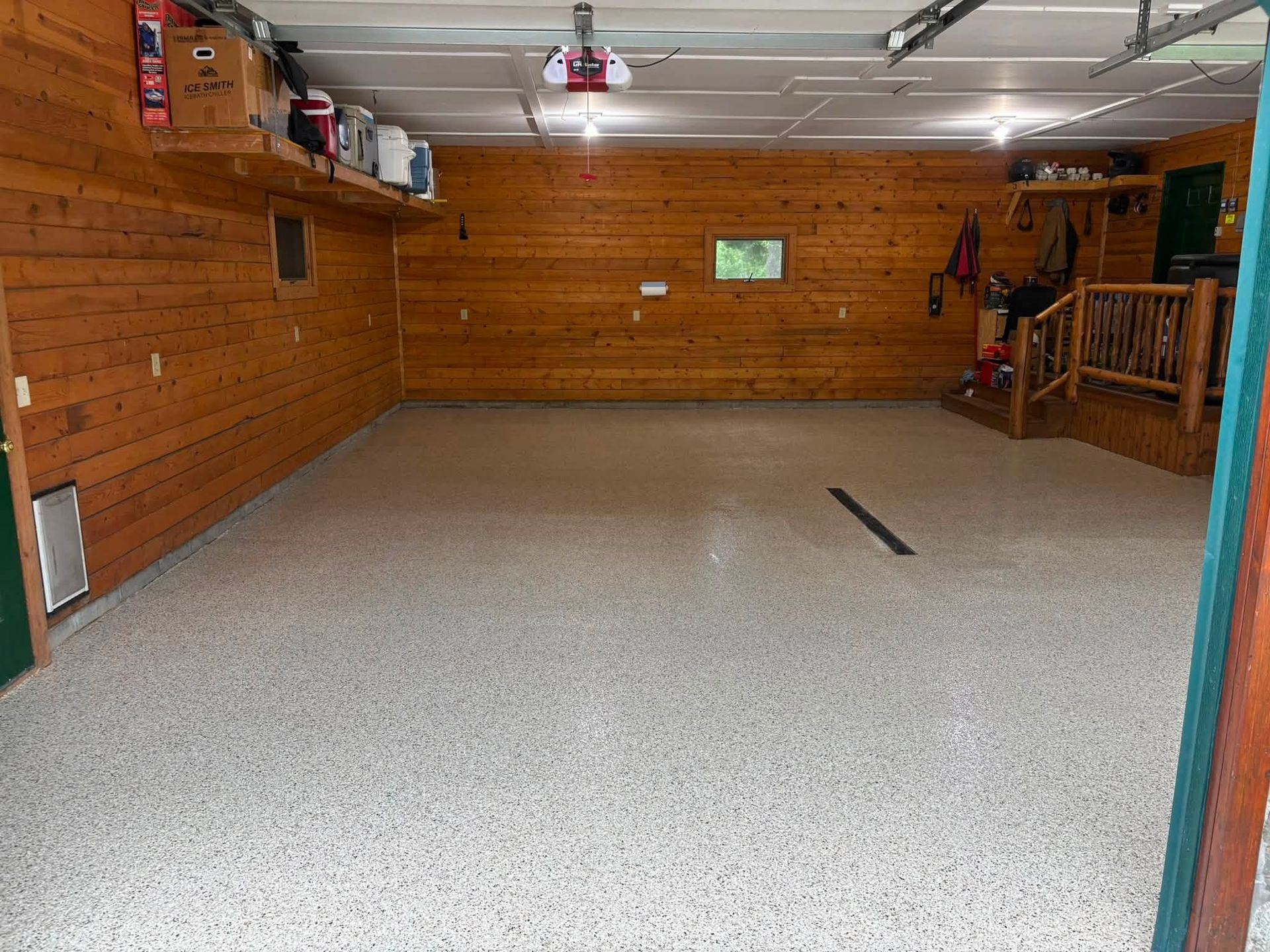 Empty garage with wood-paneled walls, speckled floor, overhead lights, and a small window.