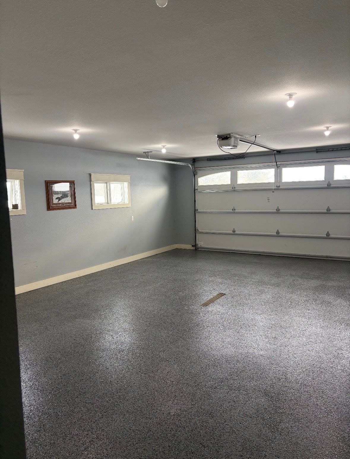 Empty gray garage with speckled floor, white ceiling lights, and a closed garage door.