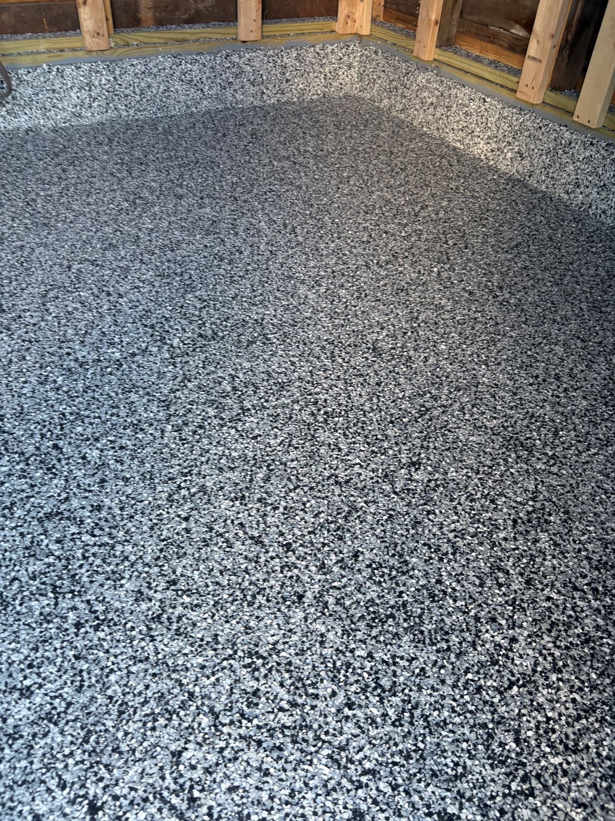 Speckled gray epoxy floor in an unfinished room with exposed wooden framing