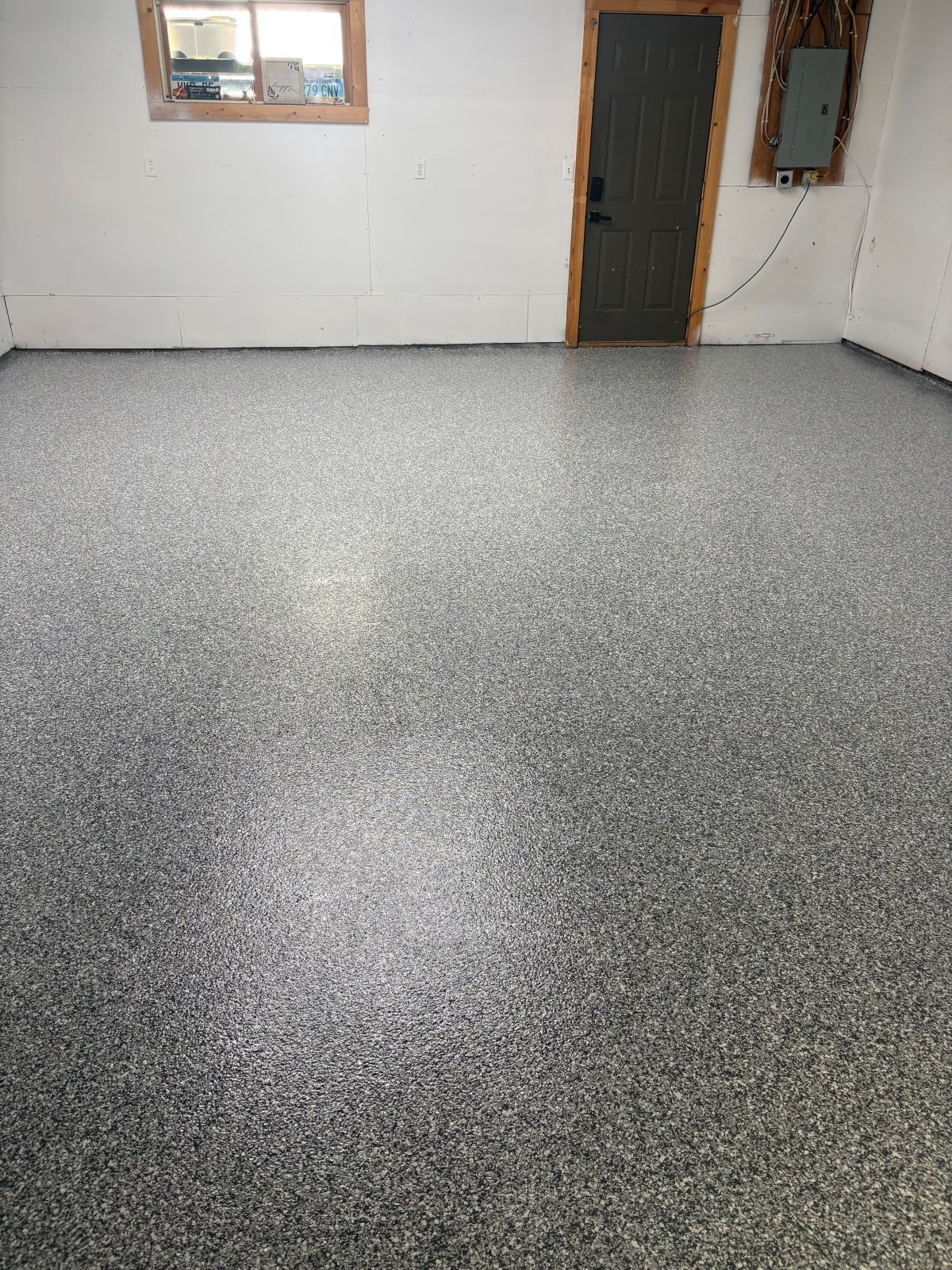 Empty room with speckled gray floor, white walls, a dark door, and two windows.