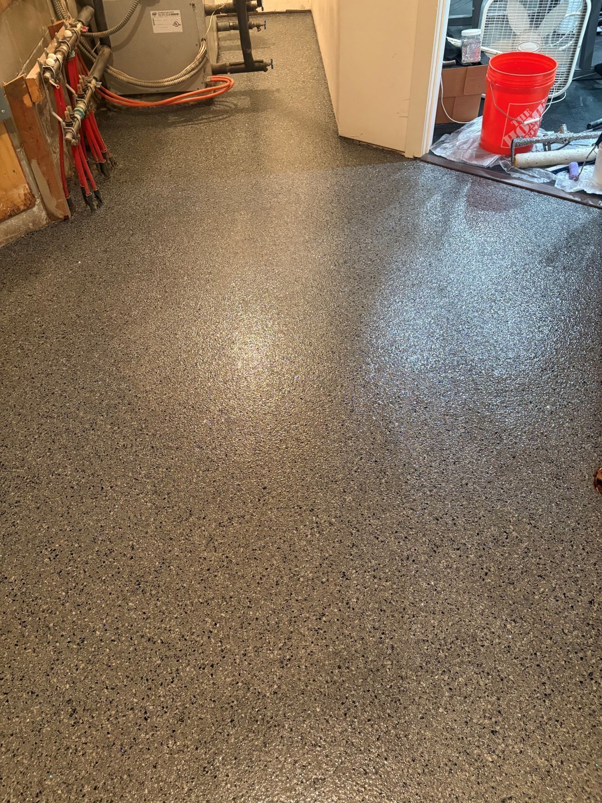 Speckled gray garage floor with a red bucket and tools near the wall