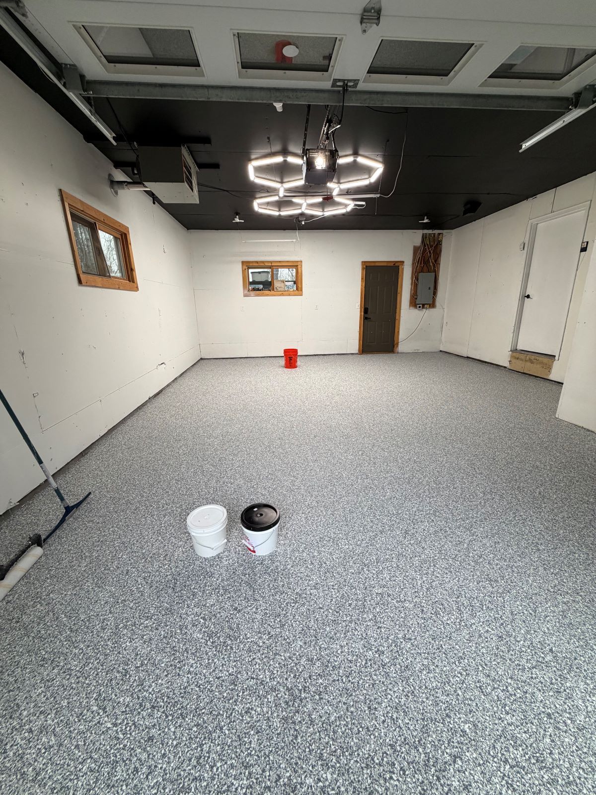 Empty garage with speckled floor, exposed ceiling lights, and two paint buckets in the foreground.