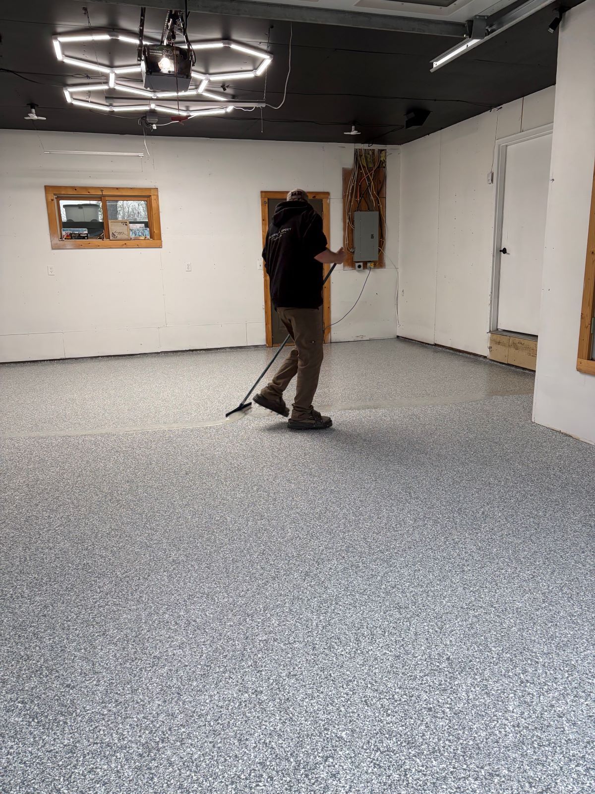 Person walking in a mostly empty room with white walls, gray carpet, and ceiling lights.