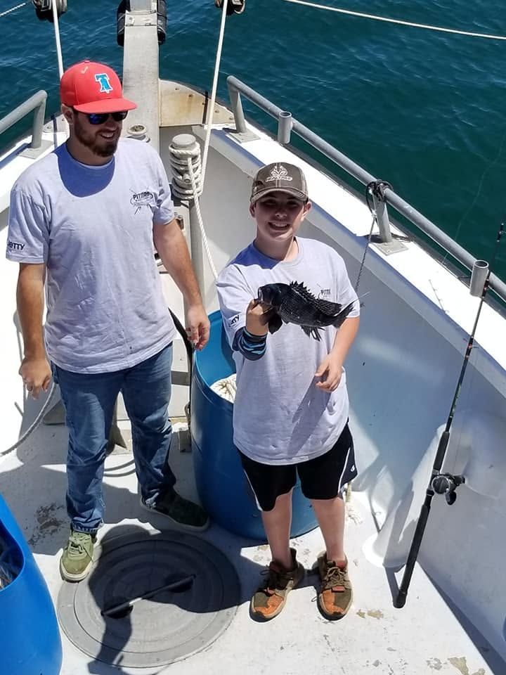 Two people on a boat deck holding a fish, with blue water in the background.