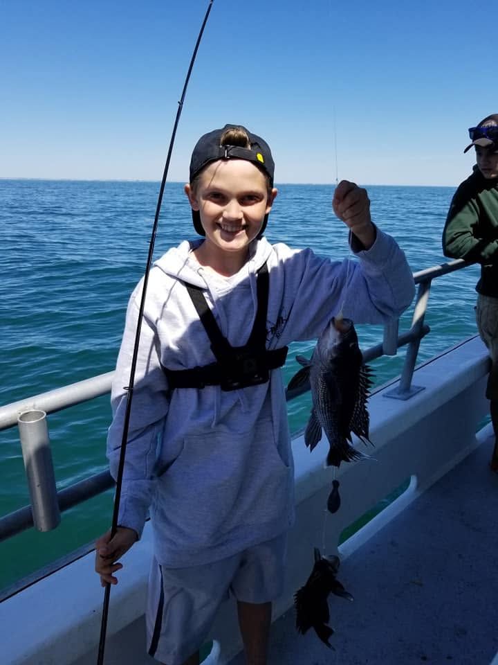 Young person on a boat holding a fishing rod and a freshly caught fish on a sunny day at sea