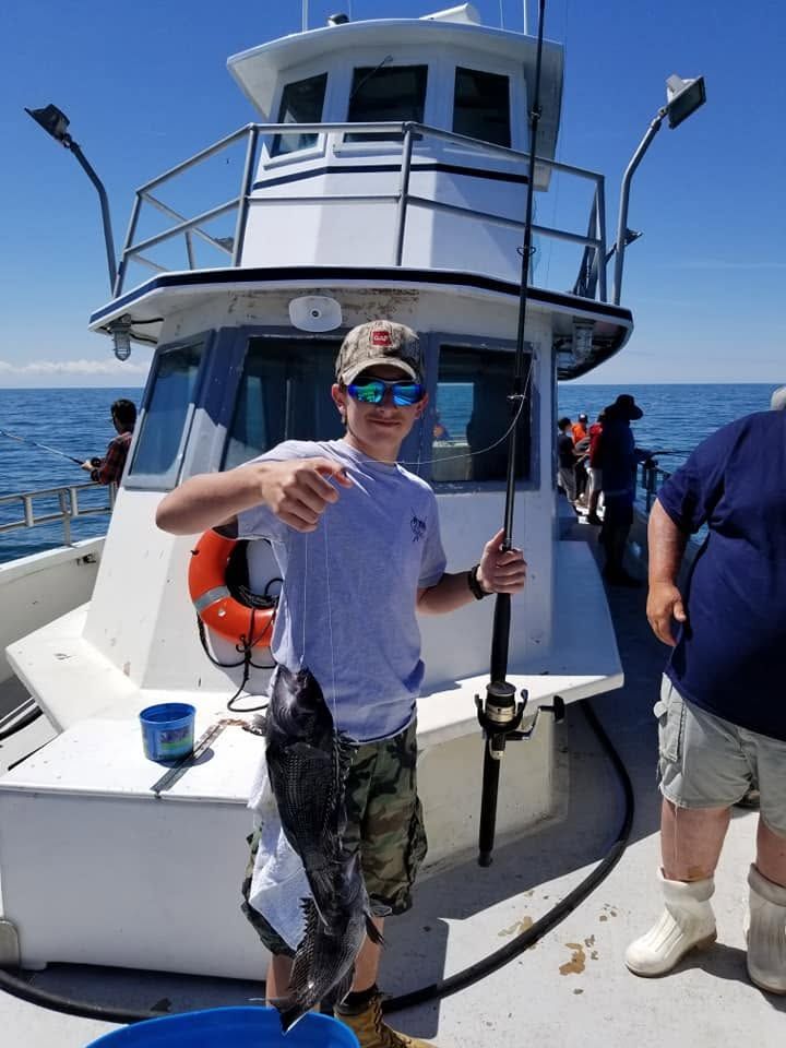 Person holding up a fish on a boat deck, with ocean and blue sky in the background.